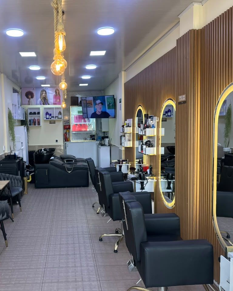 Interior de Maquiavelo's Hair Studio: pasillo con sillas de corte negras, espejos con luz dorada y lámparas colgantes