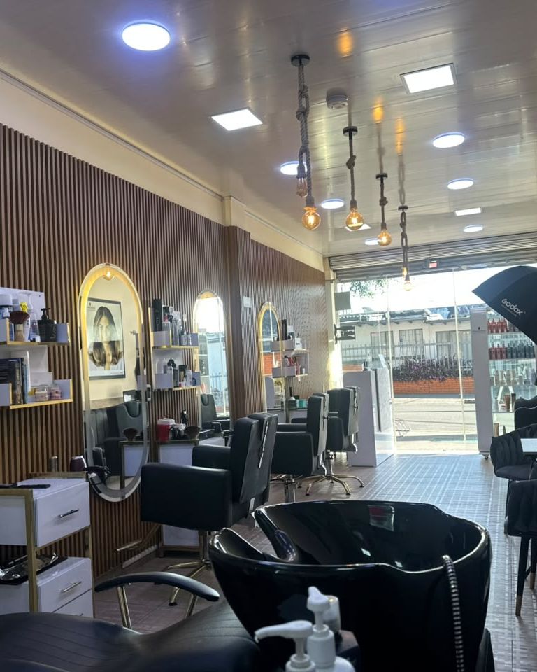 Interior de Maquiavelo's Hair Studio: puestos de corte con espejos ovalados, pared de listones de madera y lámparas colgantes