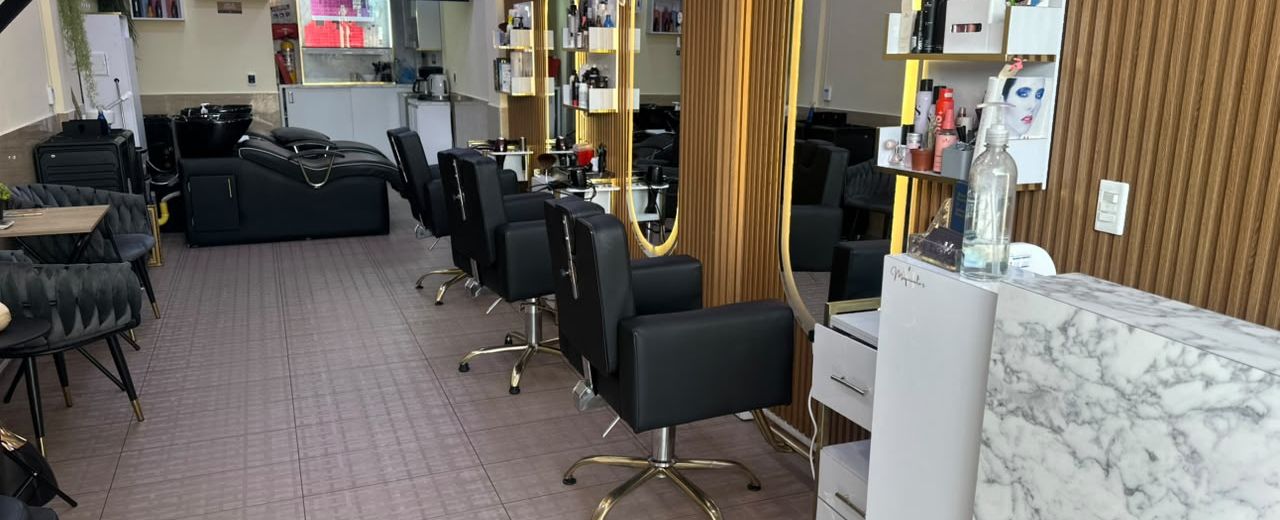 Puestos de corte con sillas negras de base dorada, espejos iluminados y mostrador de mármol en Maquiavelo's Hair Studio
